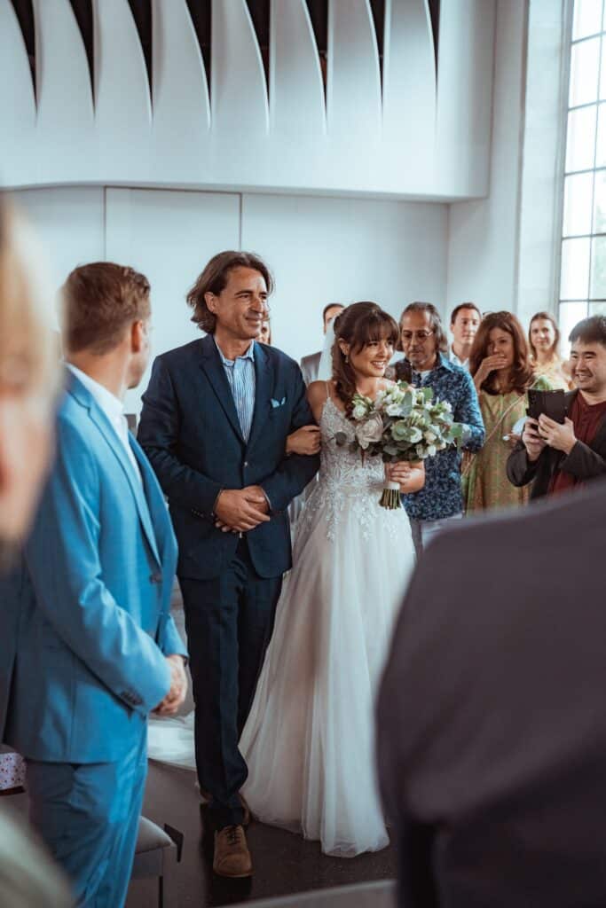Braut geht mit Begleiter zum Altar durch Gäste.