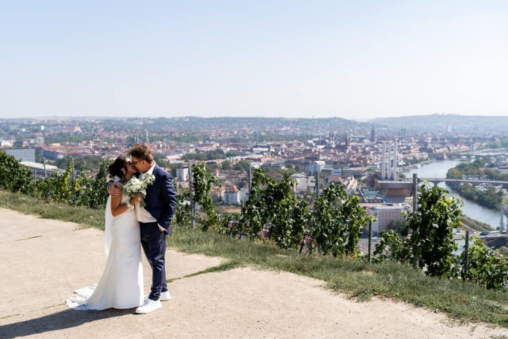 Brautpaar küsst sich vor Stadtpanorama im Weinberg