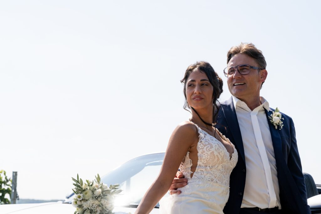 Brautpaar lächelnd vor Hochzeitsauto im Freien