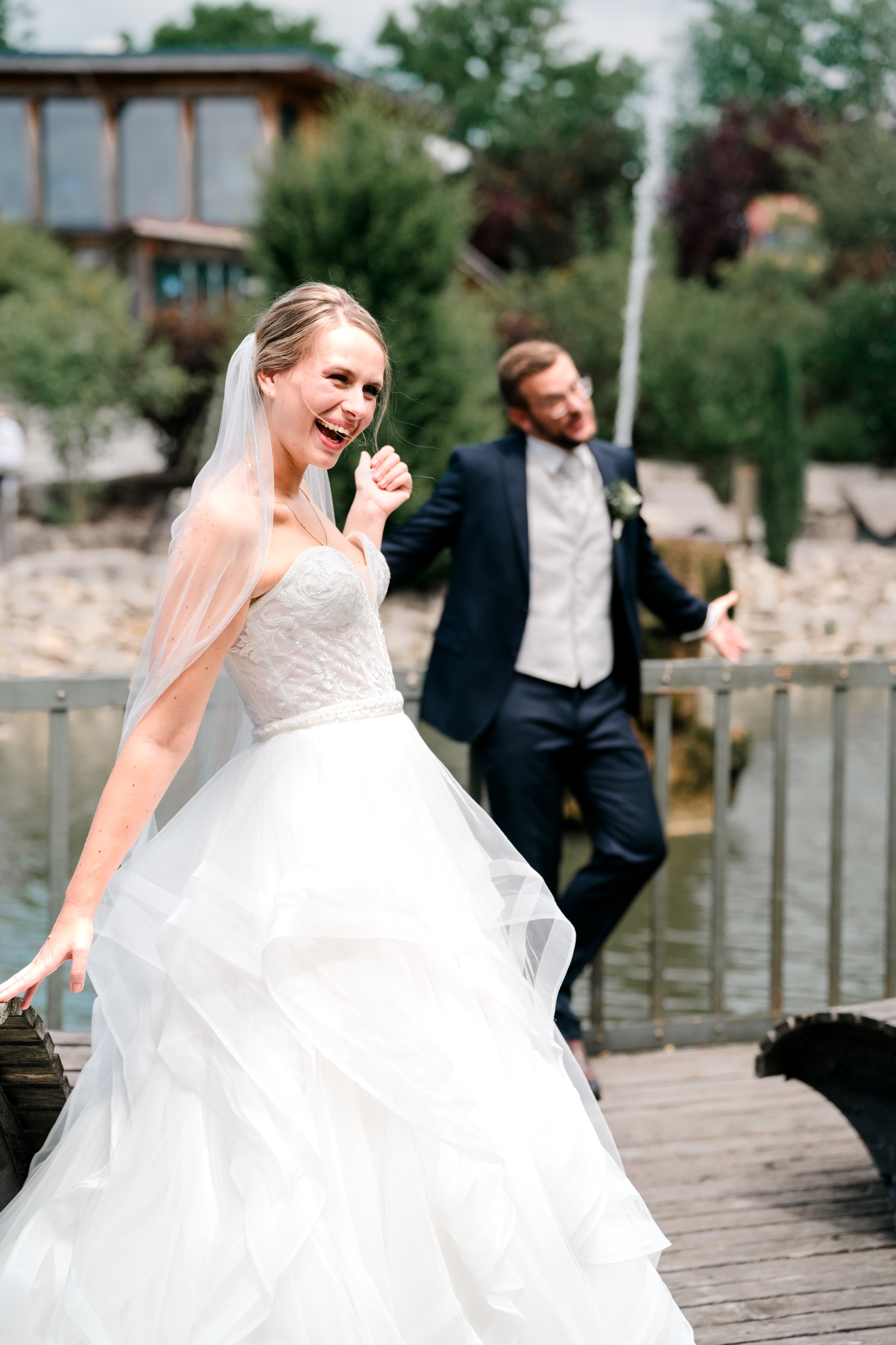 Brautpaar lacht auf Holzbrücke vor Teich