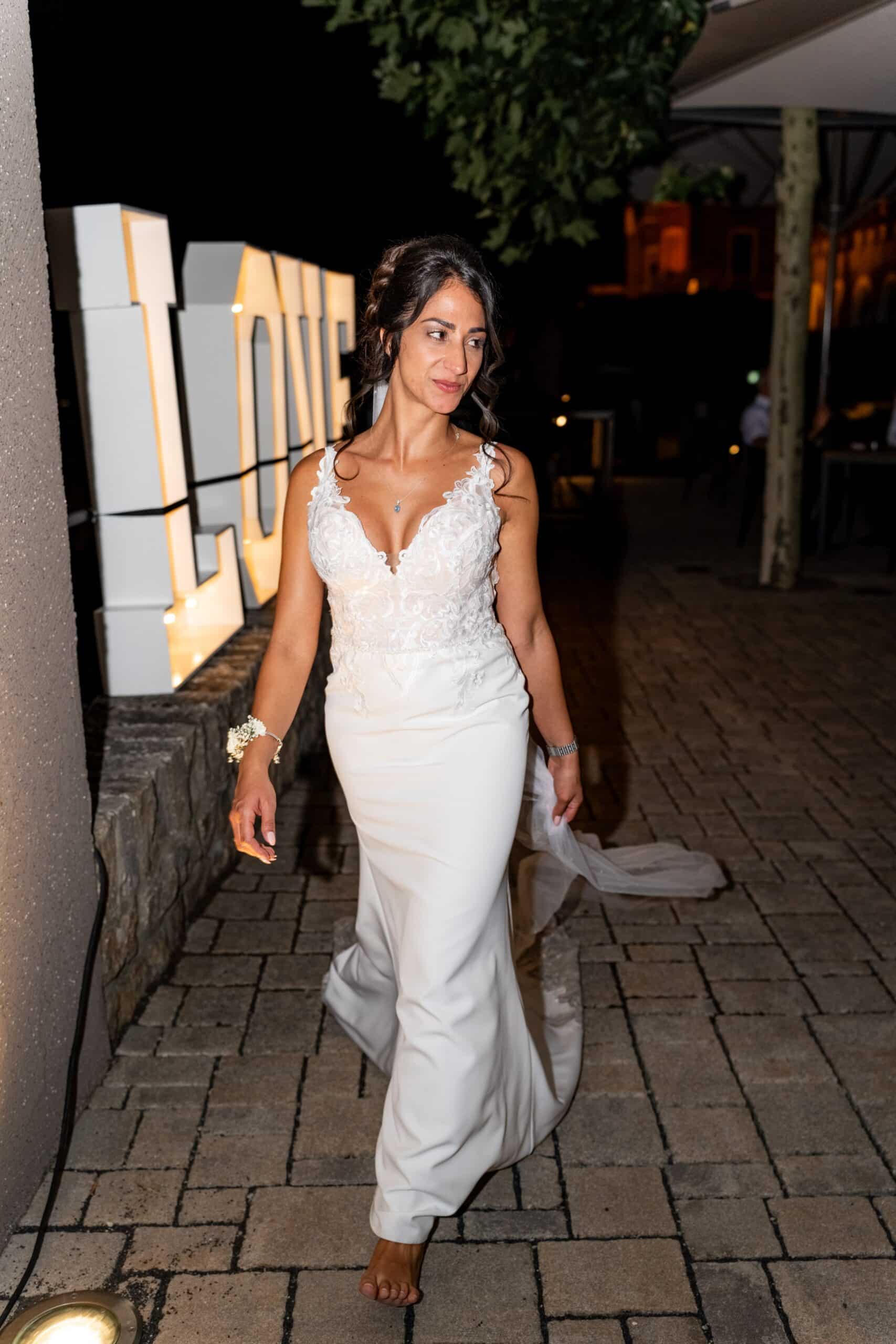 Braut in Abendkleid neben Leuchtschrift LOVE