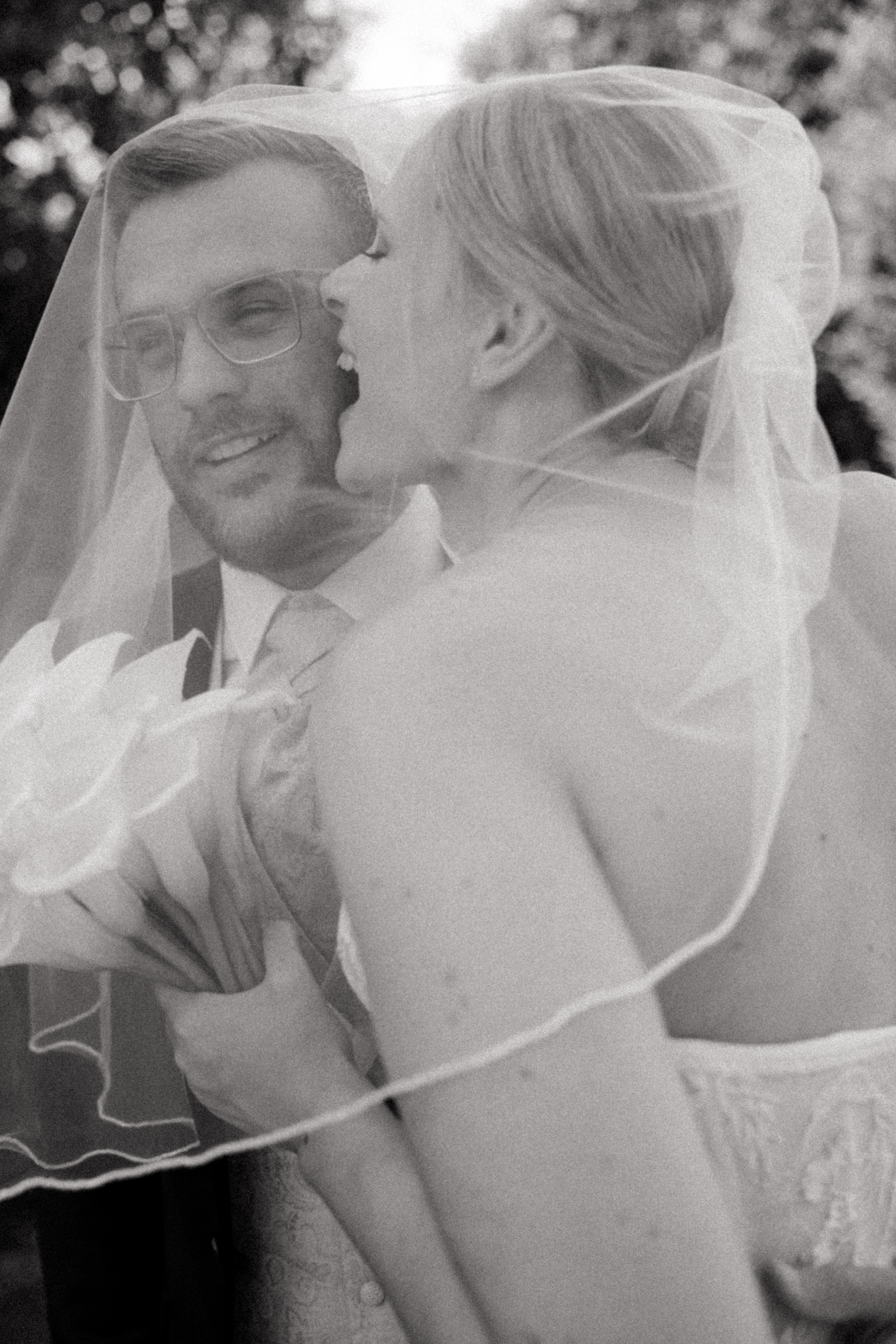 Brautpaar unter gemeinsamem Schleier im Garten.