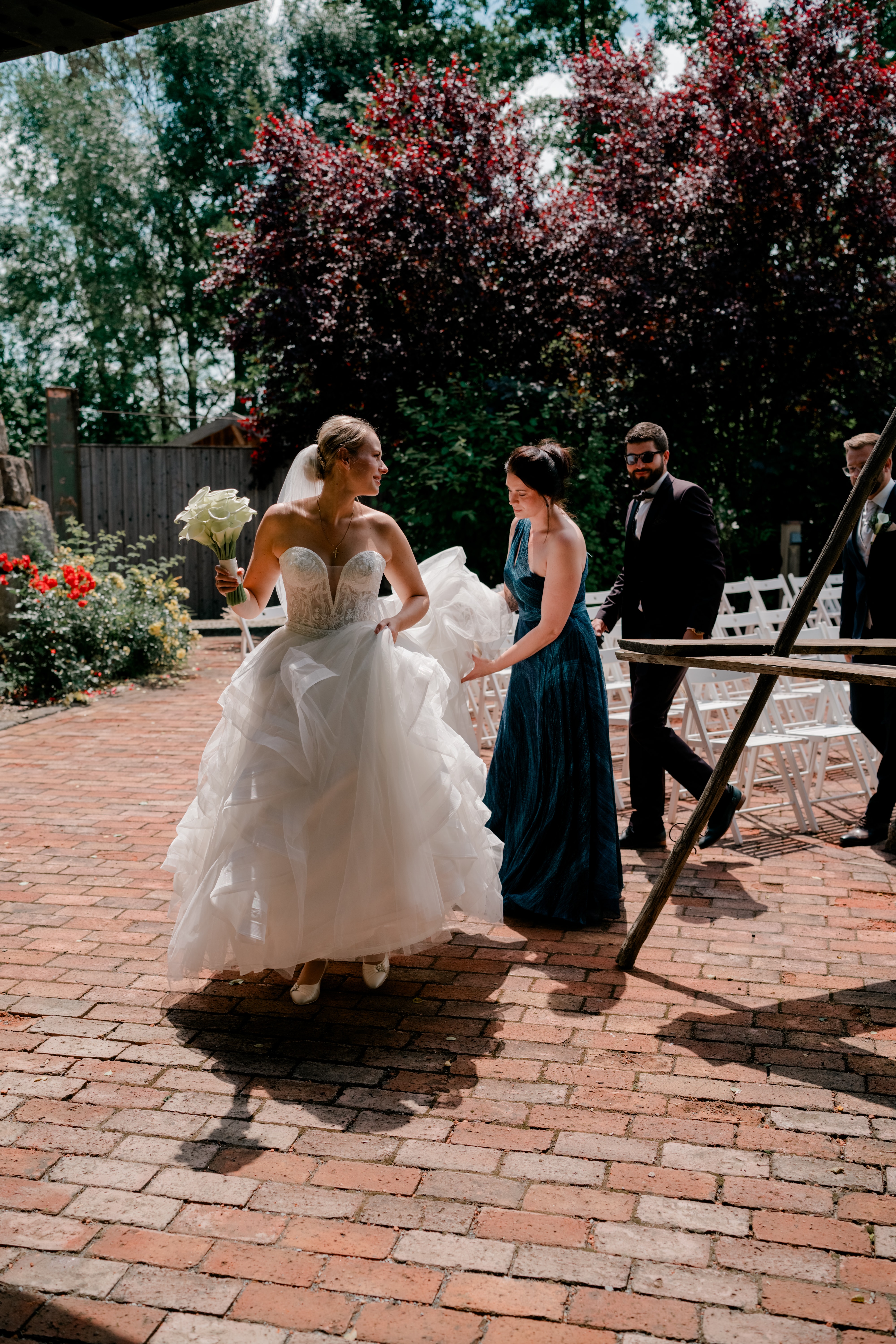 Braut im Garten mit Brautjungfer und Gästen