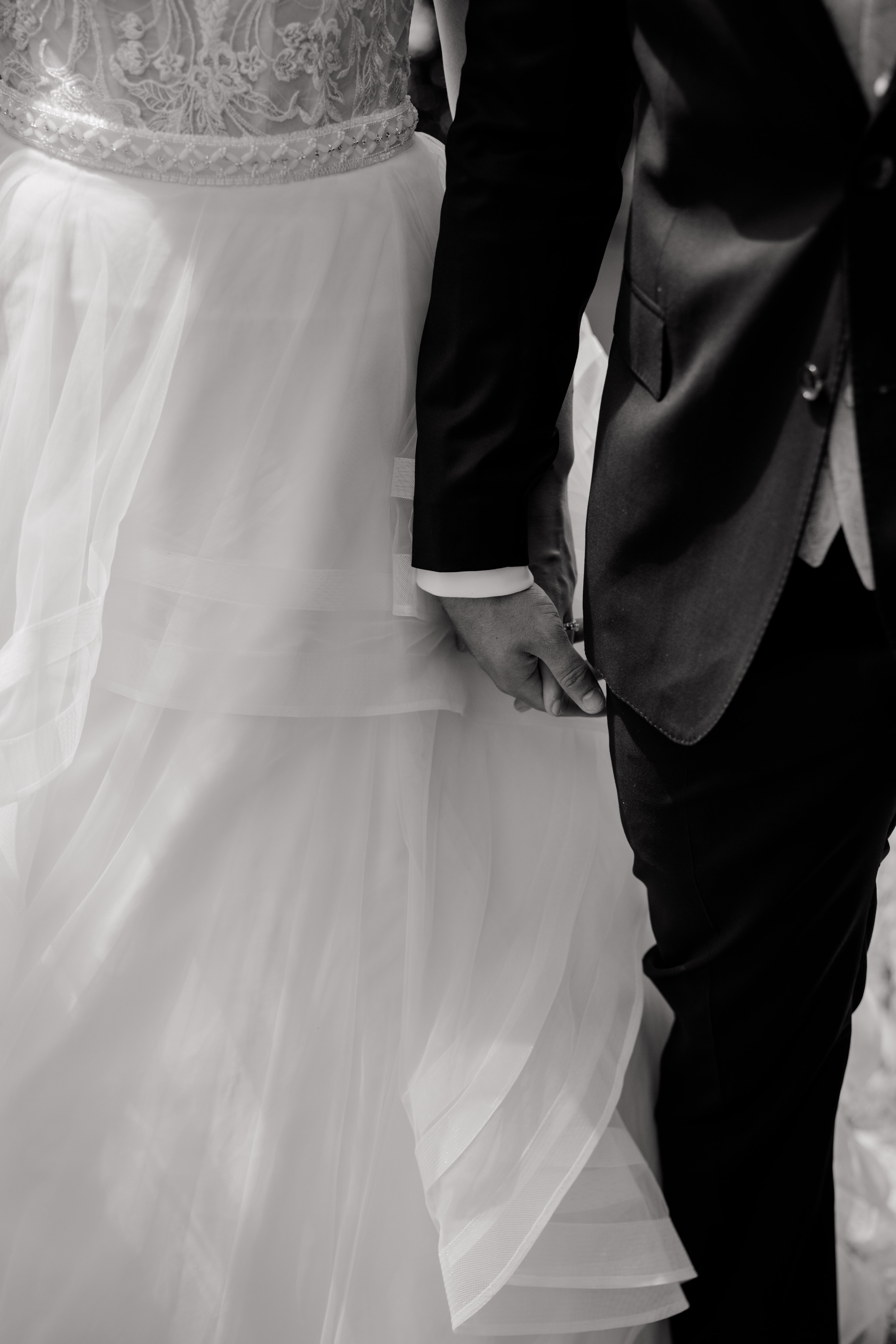 Brautpaar hält Hände in eleganter Hochzeitskleidung