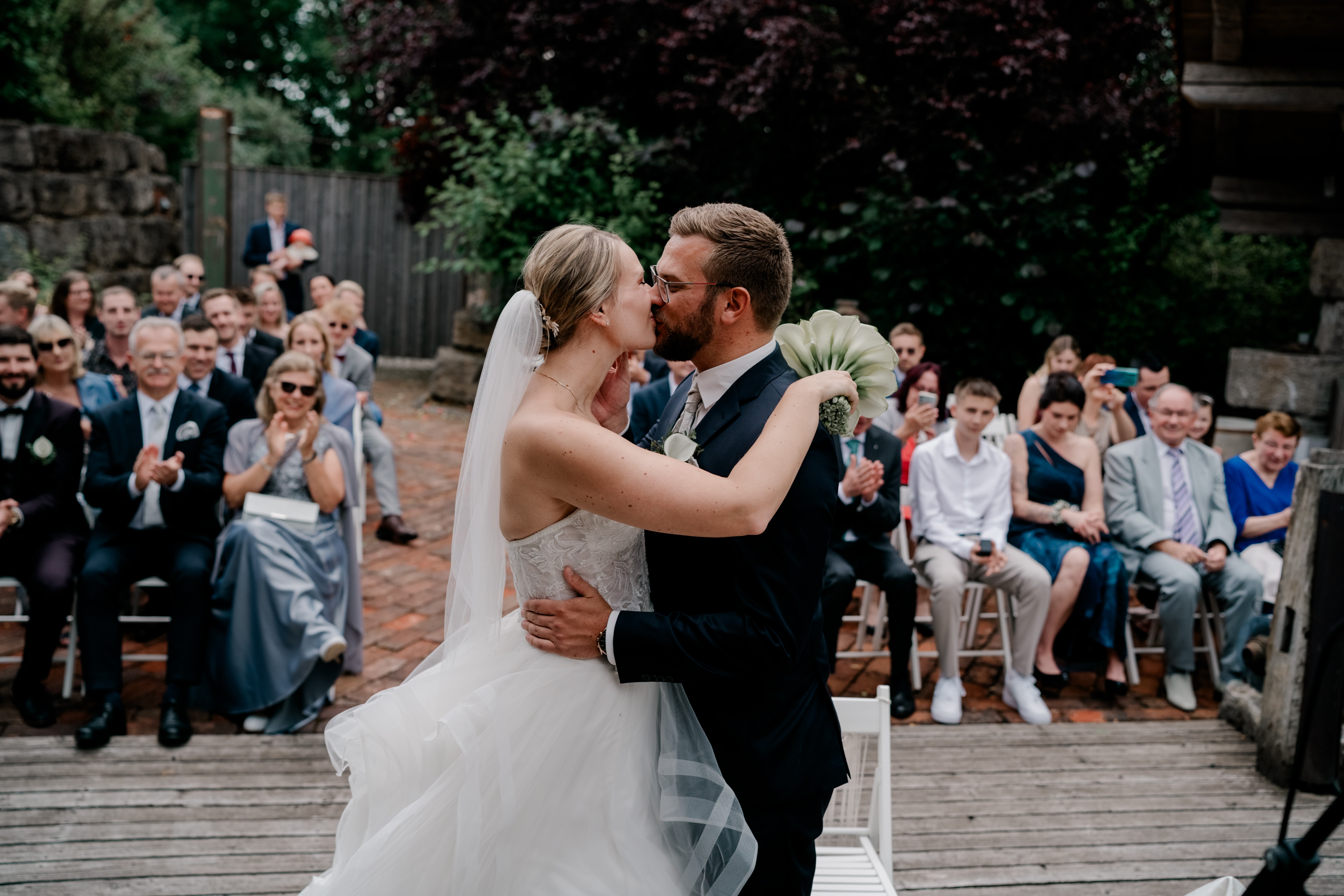 Brautpaar küsst sich vor applaudierenden Gästen