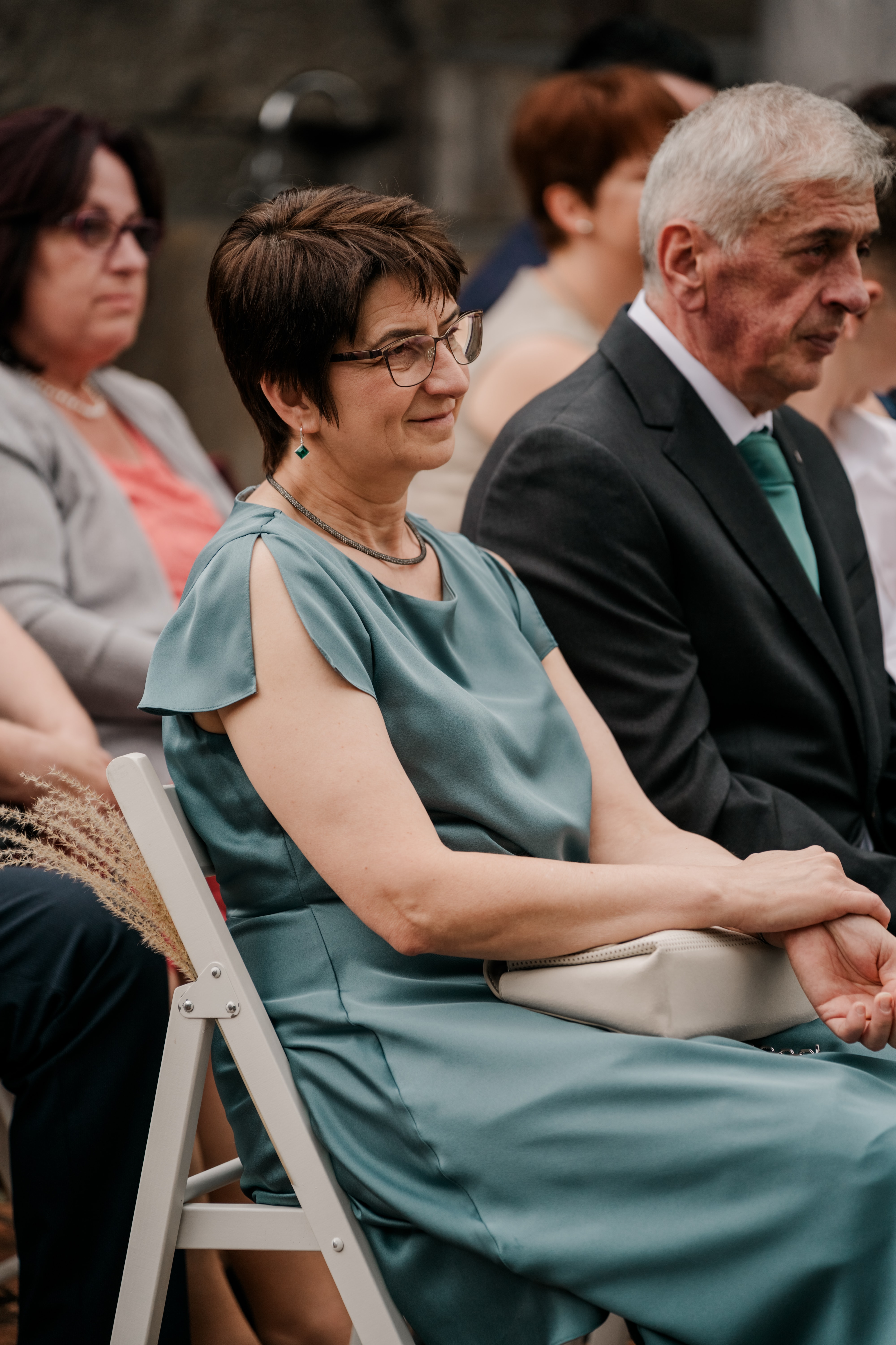 Hochzeitsgäste in festlicher Kleidung auf Stühlen