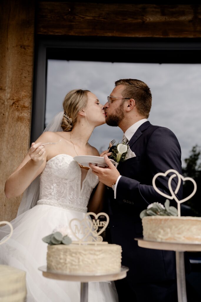 Brautpaar küsst sich beim Anschneiden der Hochzeitstorte