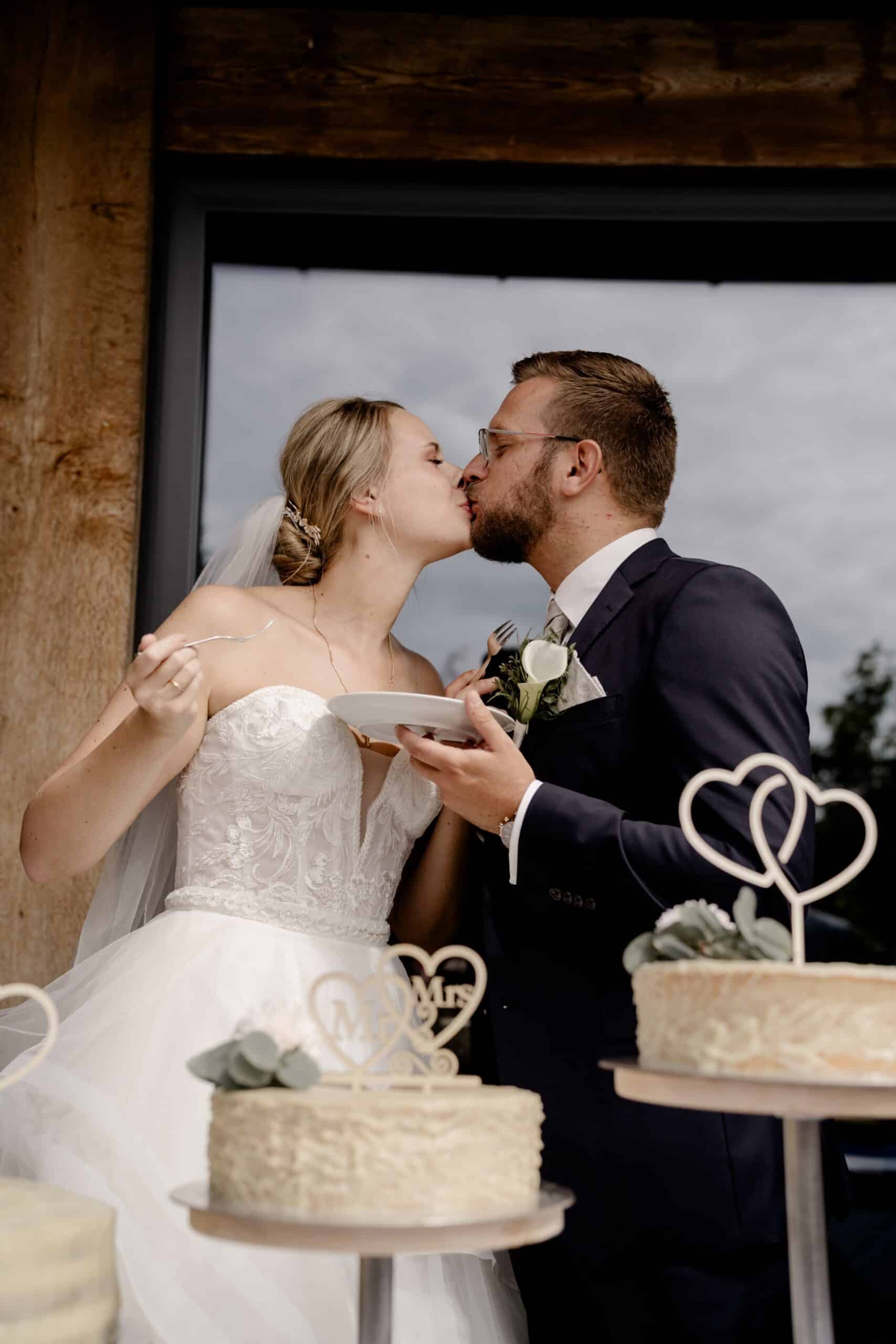 Brautpaar küsst sich beim Anschneiden der Hochzeitstorte