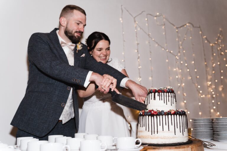 00612-florian-knusper-hochzeitsfotograf-wuerzburg-brautpaar-schneidet-hochzeitstorte-Winzerhof Stahl