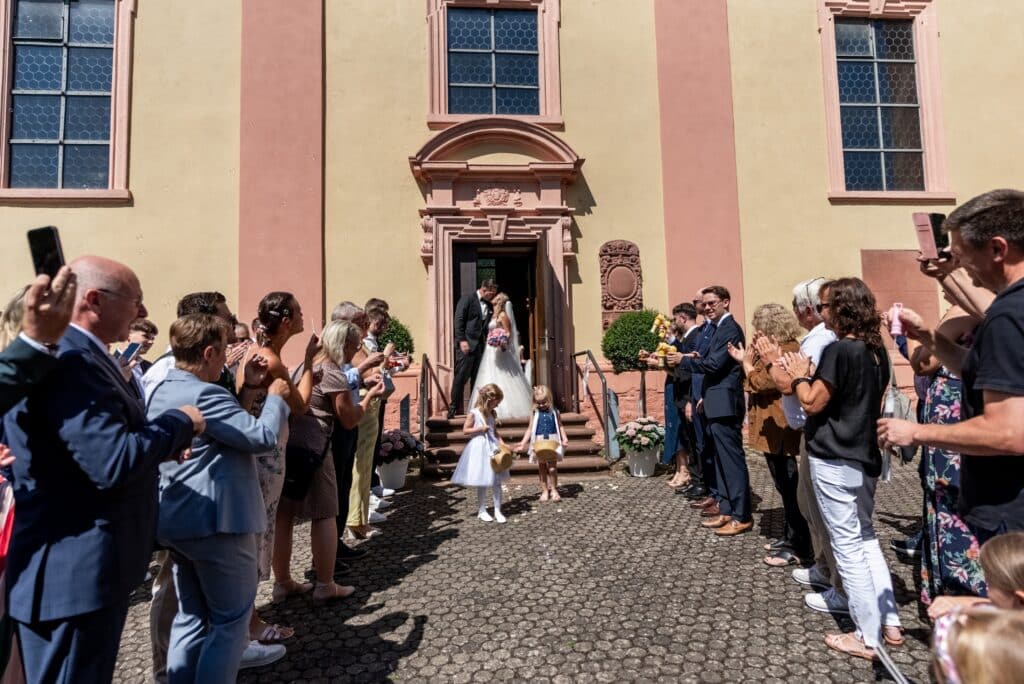 Hochzeitsgesellschaft begrüßt Brautpaar vor Kirche