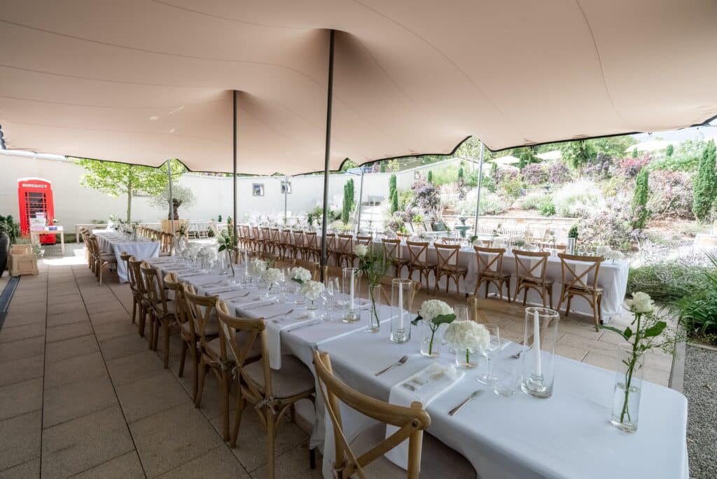 Gedeckte Hochzeitstafel im Garten mit weißen Blumen.