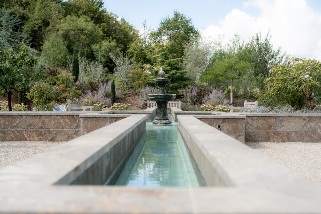 Springbrunnen im Garten mit Sitzbänken und Blumen