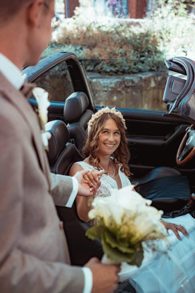 Braut im Cabrio mit Blumenstrauß und Bräutigam
