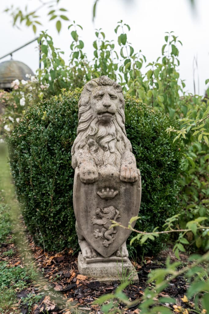 Löwenstatue im Garten mit grünen Sträuchern.