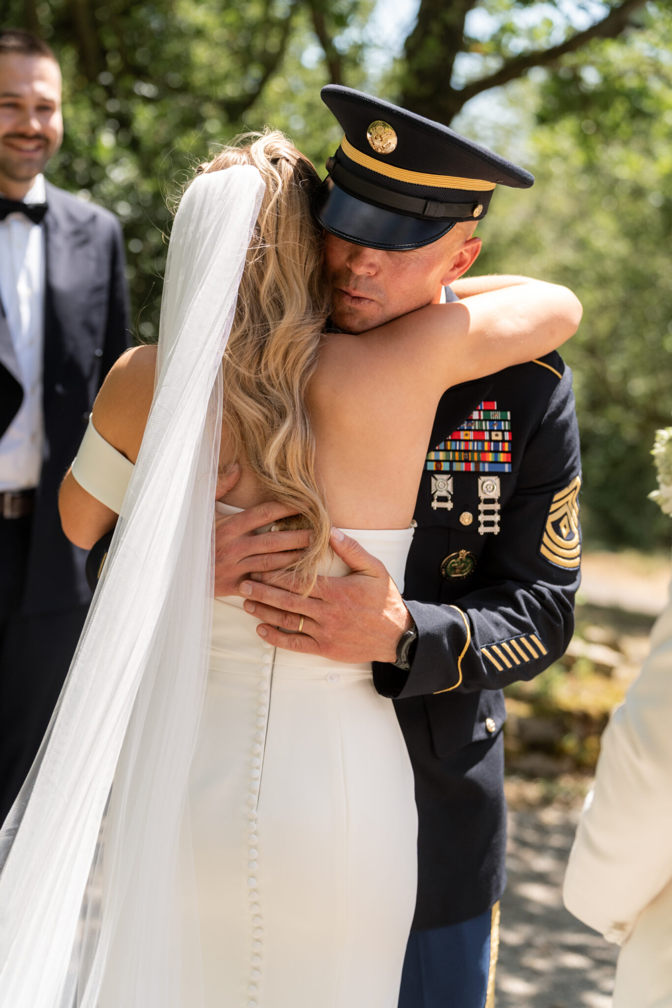 Braut umarmt Gast in Uniform bei Gartenhochzeit