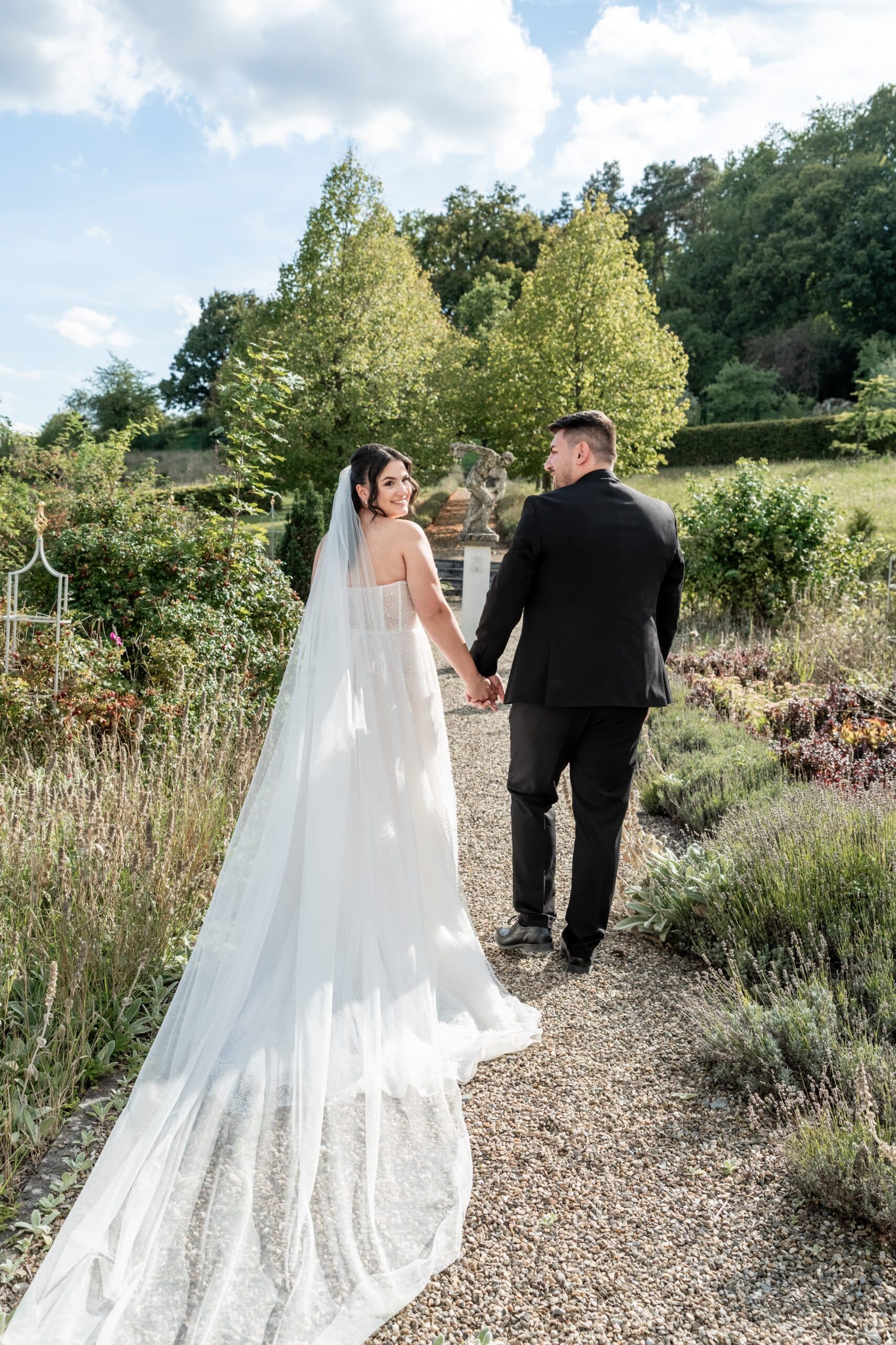 Brautpaar im Garten auf Kiesweg händchenhaltend