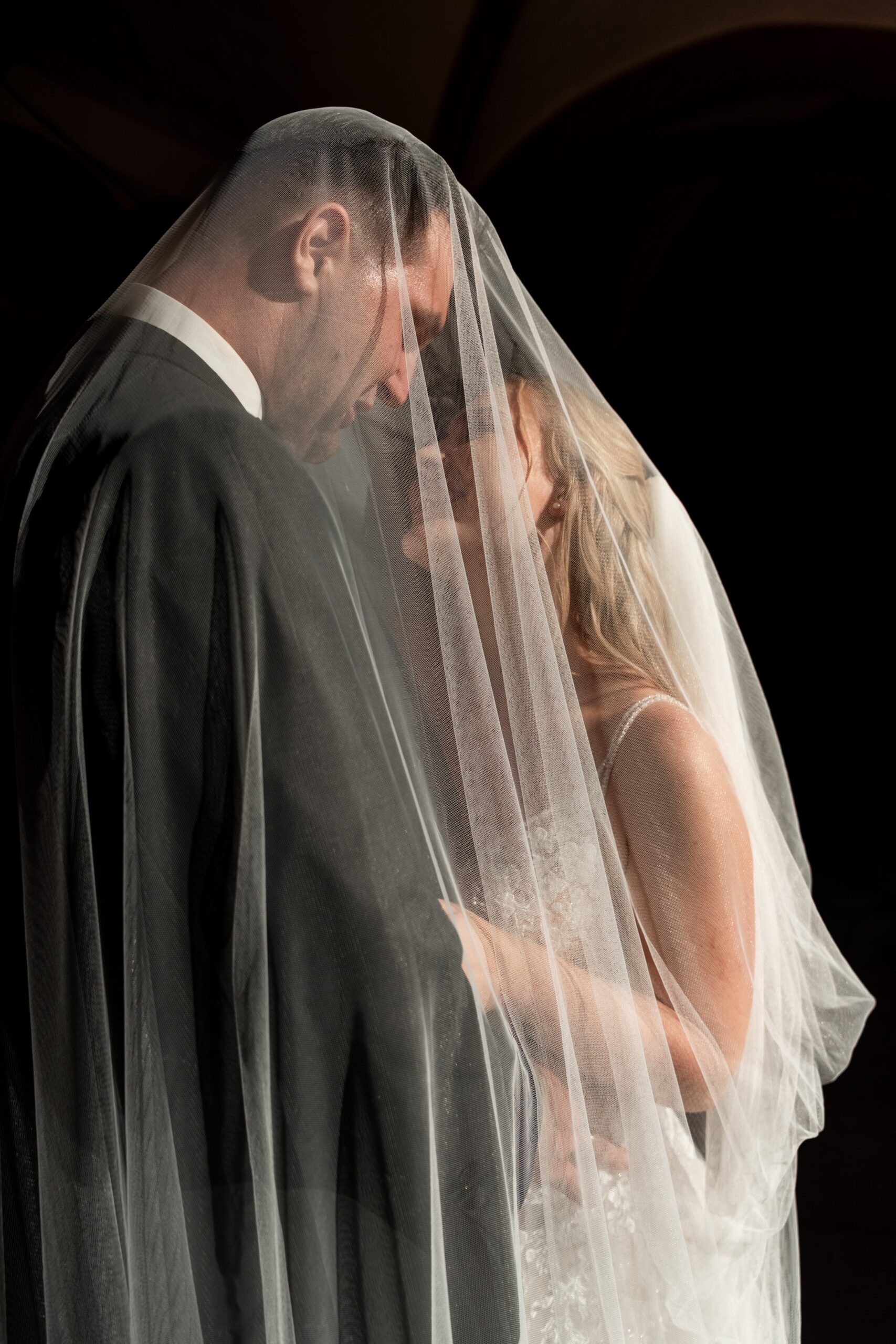 Brautpaar unter dem Schleier in inniger Umarmung