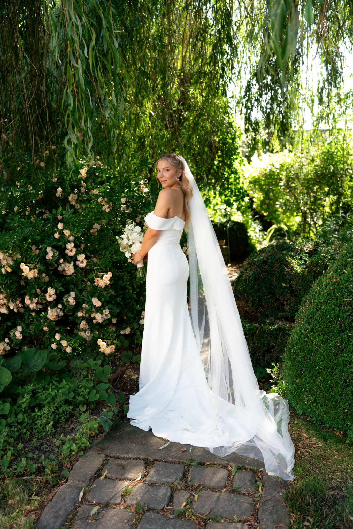 Braut im Garten mit Bouquet und langem Schleier