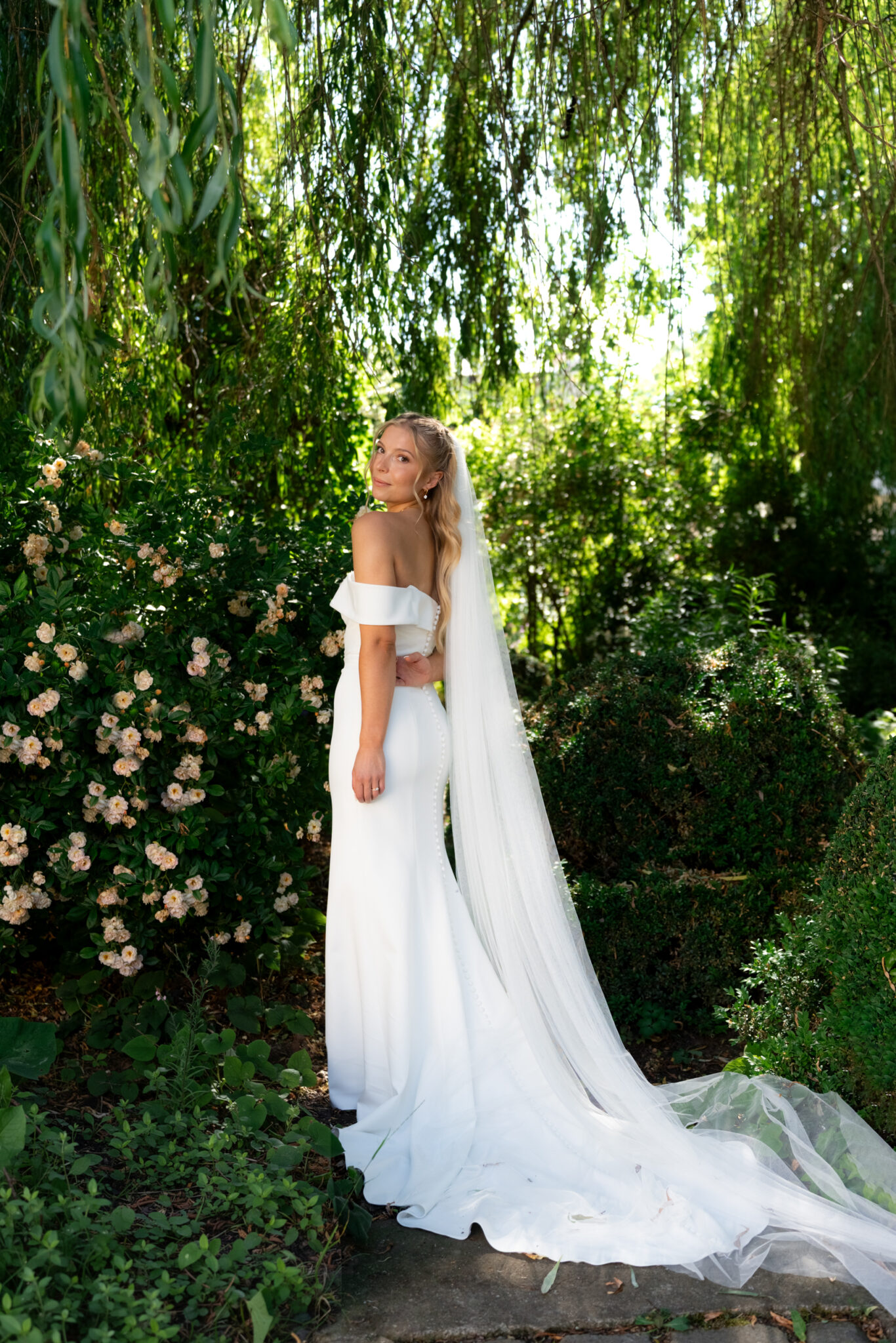 Braut im Garten mit langem Schleier und Rosen