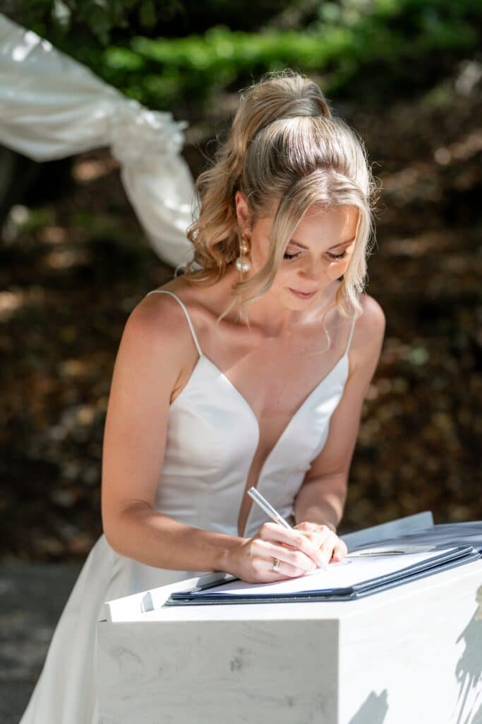 Braut unterschreibt Hochzeitsurkunde im Freien.