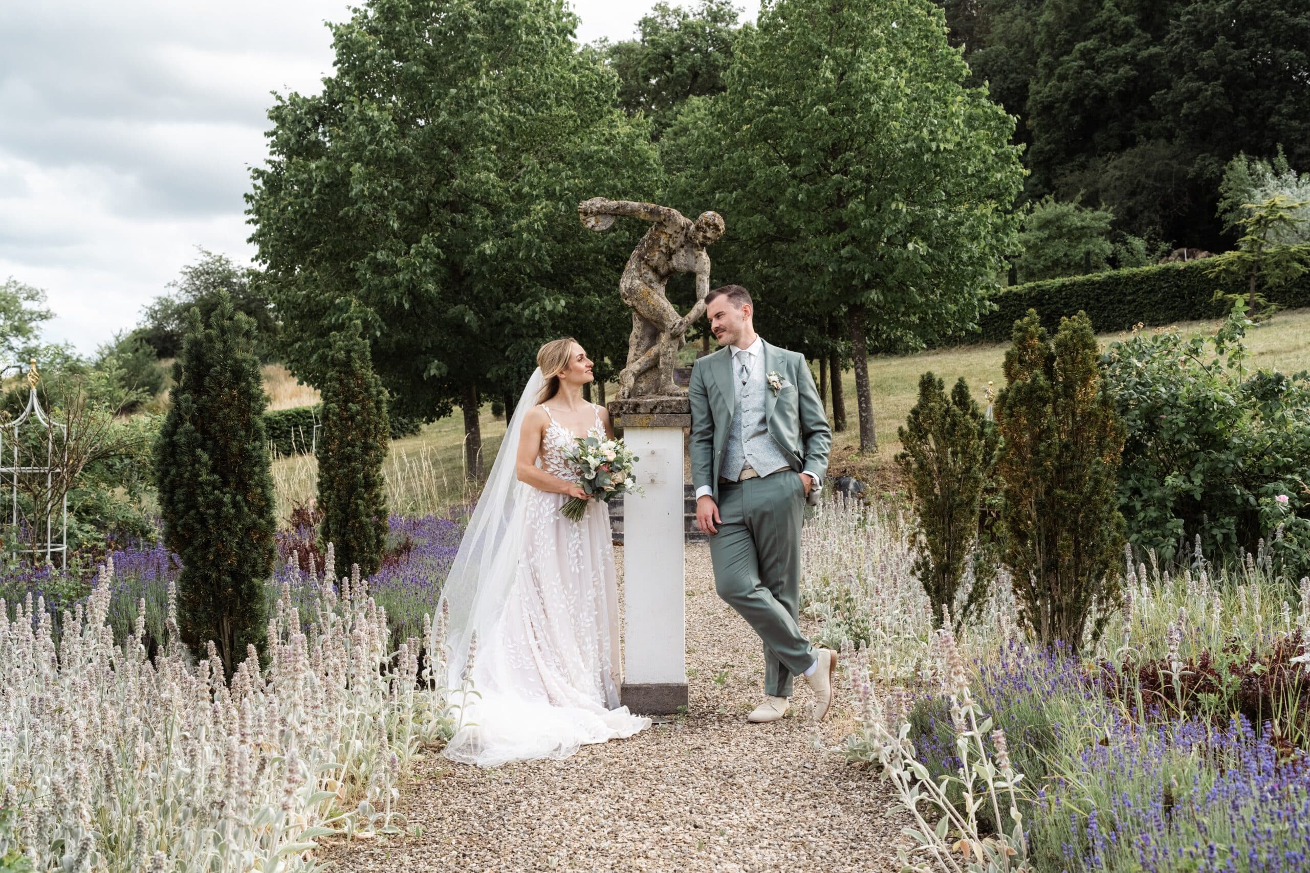 Brautpaar im Garten mit Statue und Blumenbeet