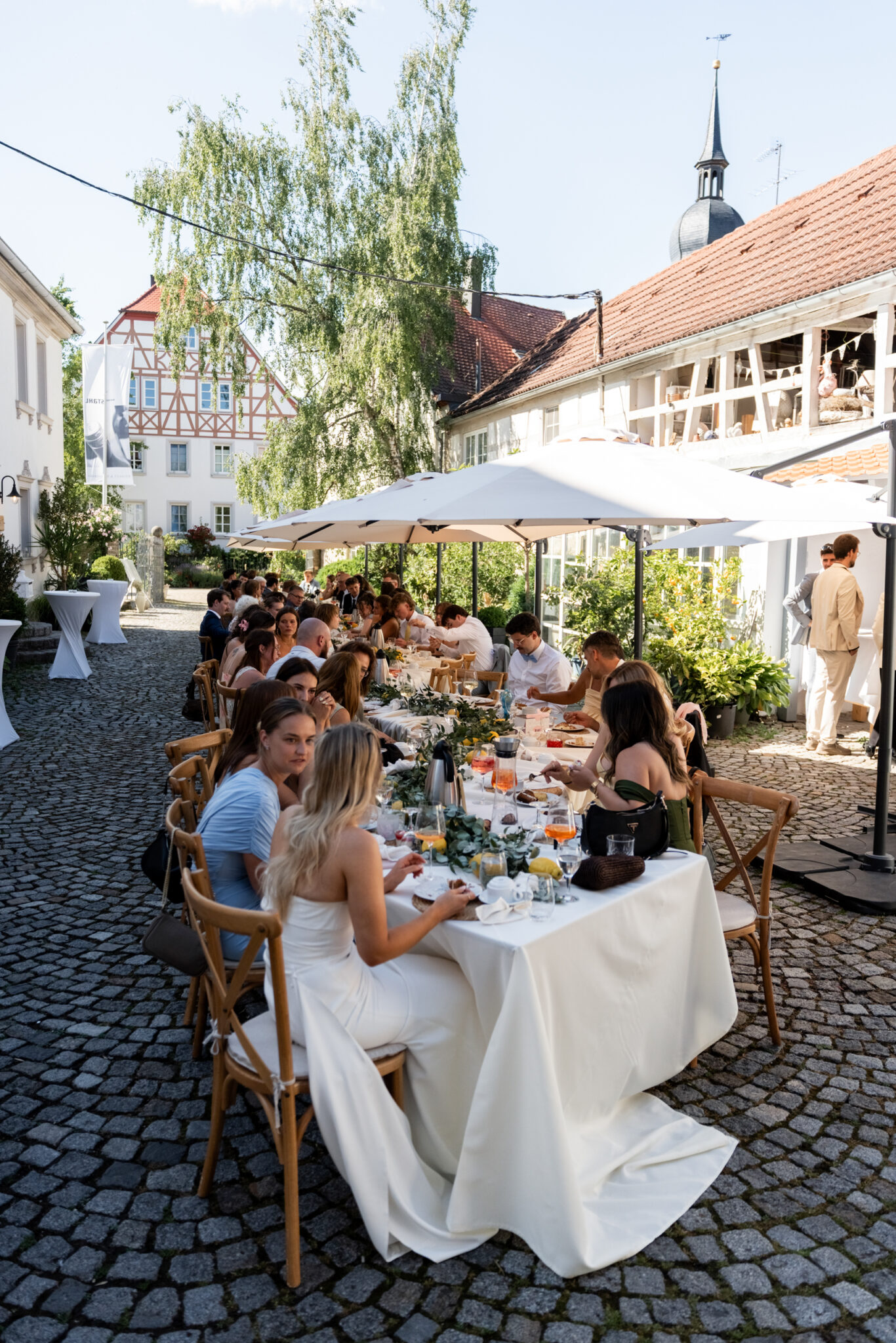 Hochzeitsgäste beim Essen im Hof unter Sonnenschirmen