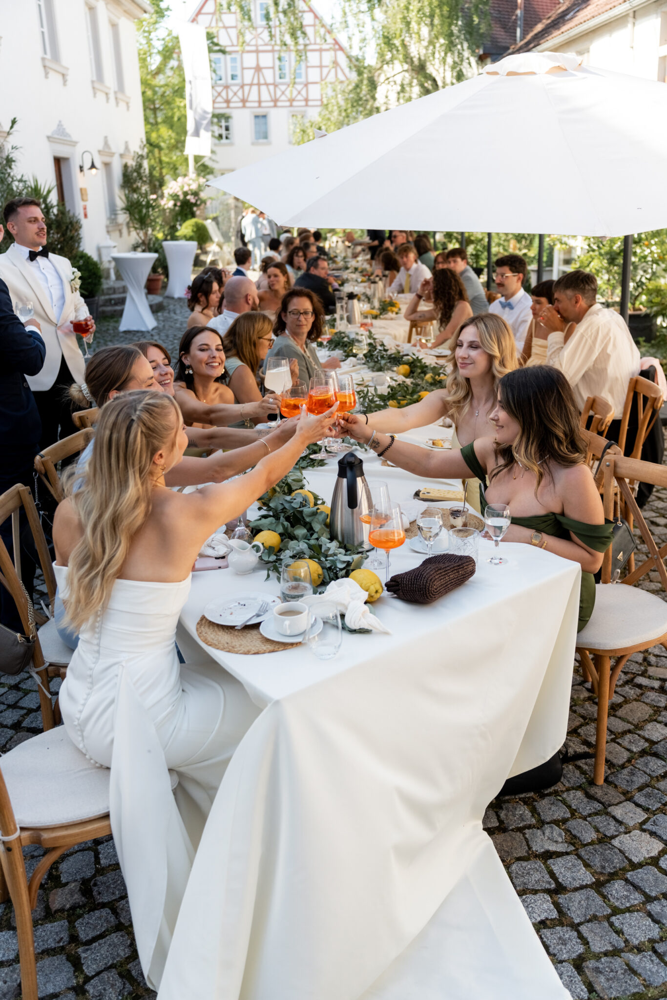 Hochzeitsgäste stoßen an langer Tafel im Freien