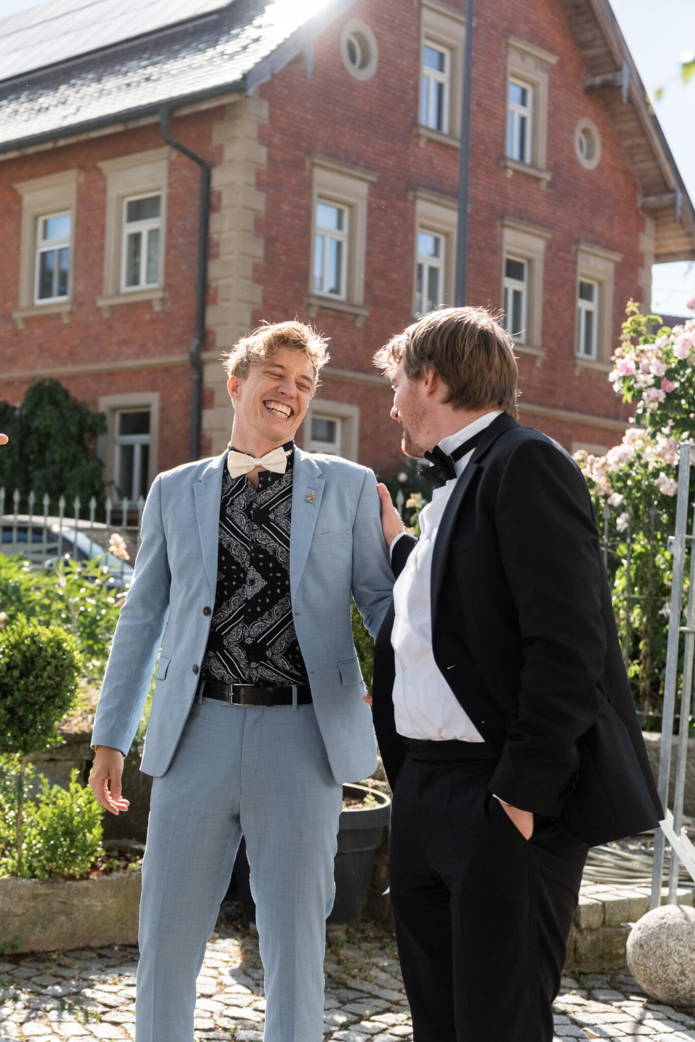 Hochzeitsgäste lachen im Hof vor Backsteinvilla