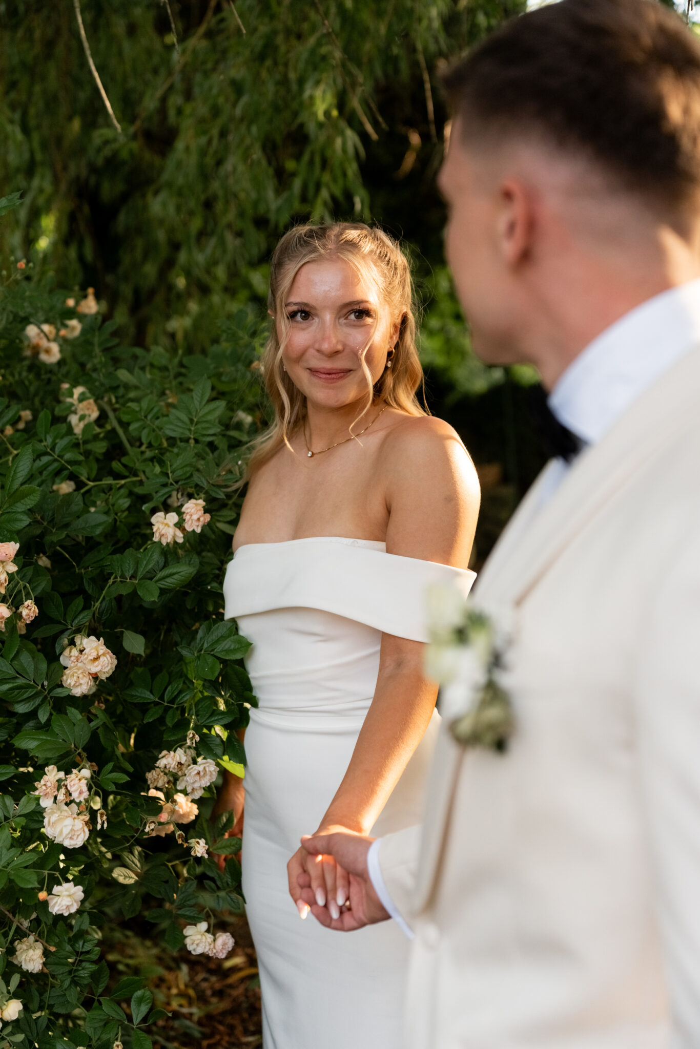 Brautpaar hält Händchen im Rosengarten bei Abendlicht