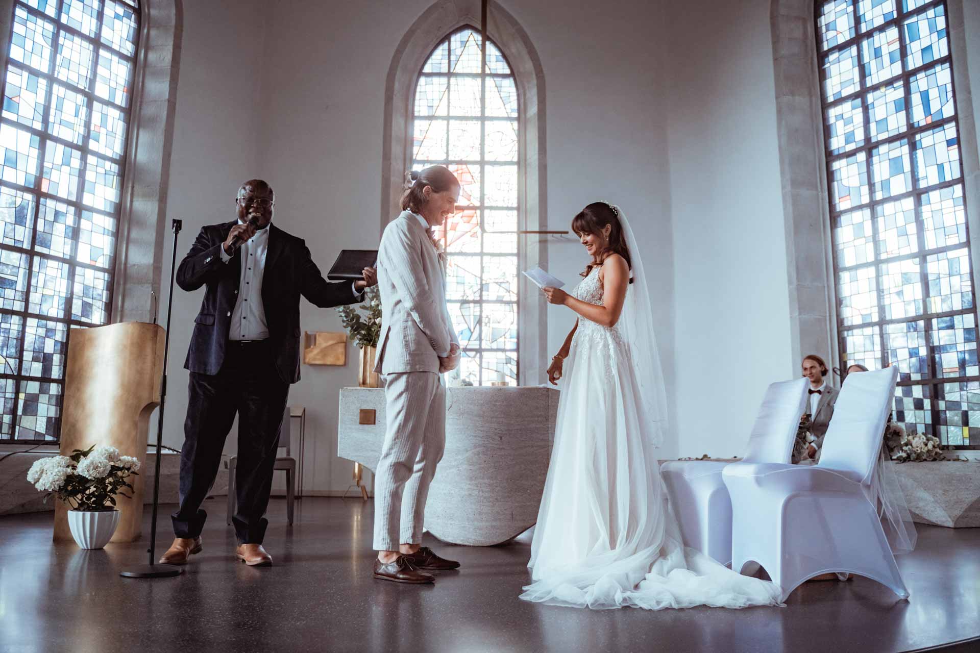 Braut und Bräutigam halten während einer Hochzeitszeremonie in einer Kirche ihre Eheversprechen, während ein Trauredner spricht.