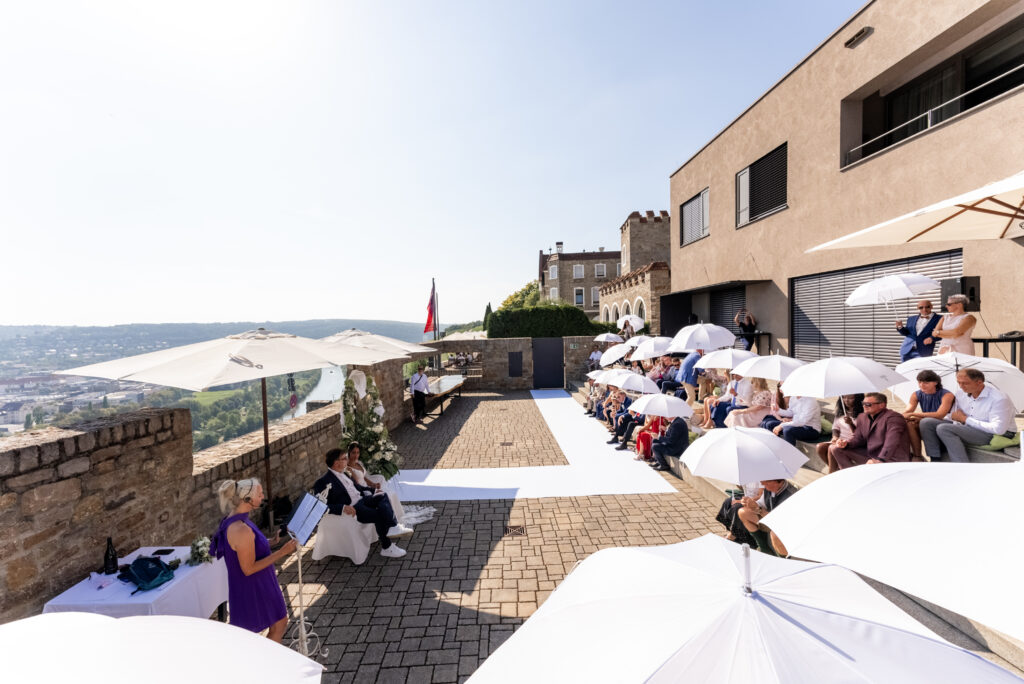 Outdoor Hochzeit mit Gästen und weißen Schirmen, romantische Zeremonie im Sonnenschein auf der Steinburg Würzburg.