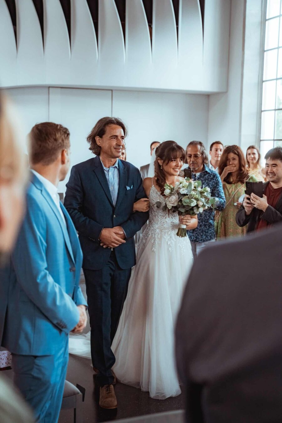 Braut geht mit Begleiter zum Altar durch Gäste.