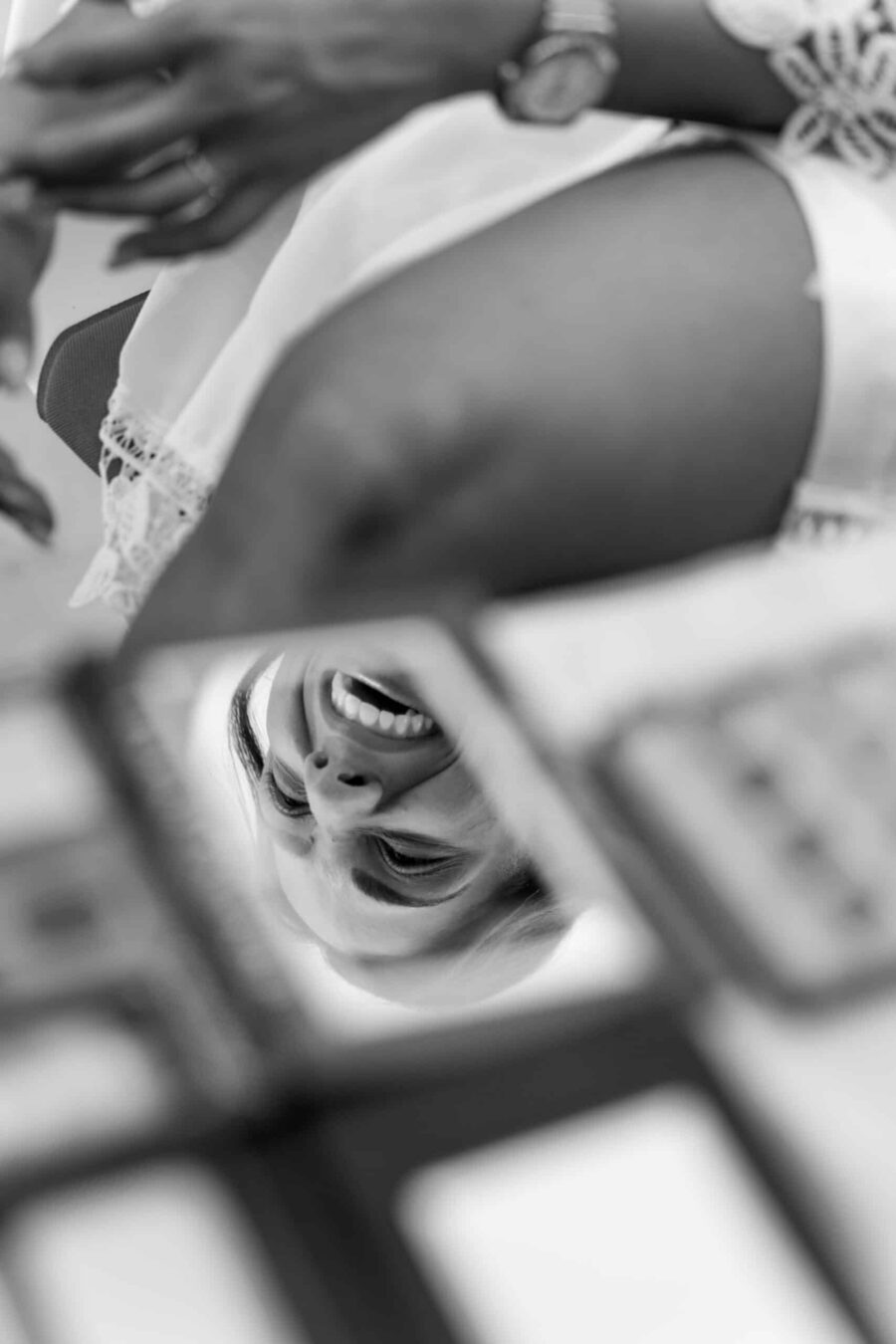 Braut lächelt in Handspiegel bei Vorbereitungen