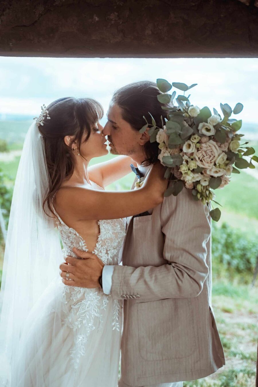 Brautpaar küsst sich im Freien mit Blumenstrauß