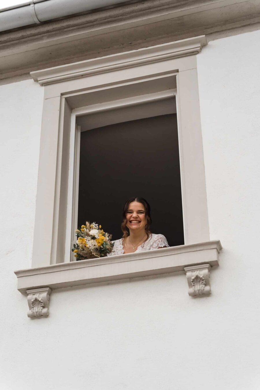 Braut mit Blumenstrauß am Fenster lächelnd