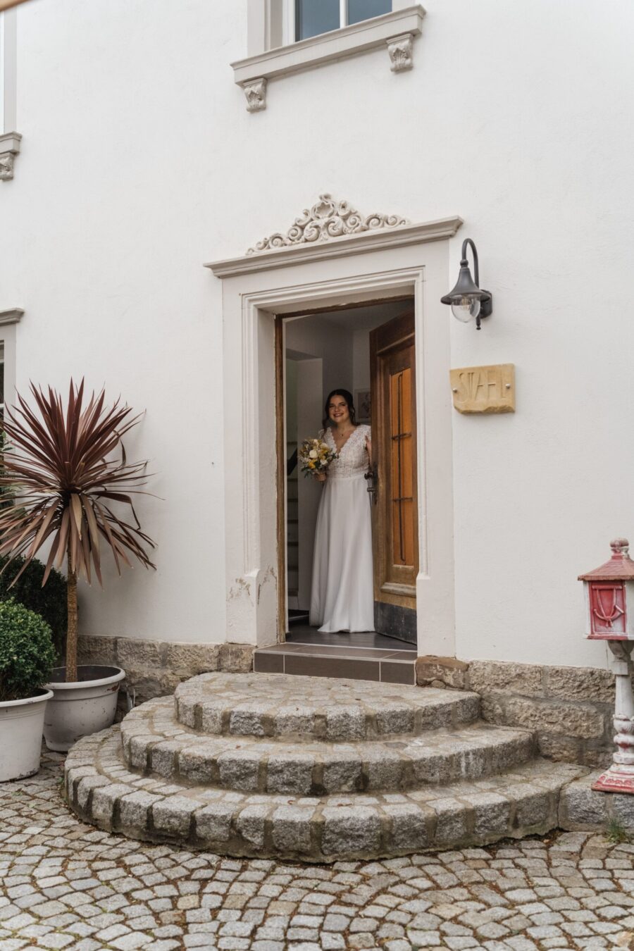 Braut mit Blumenstrauß im Eingang einer Villa.