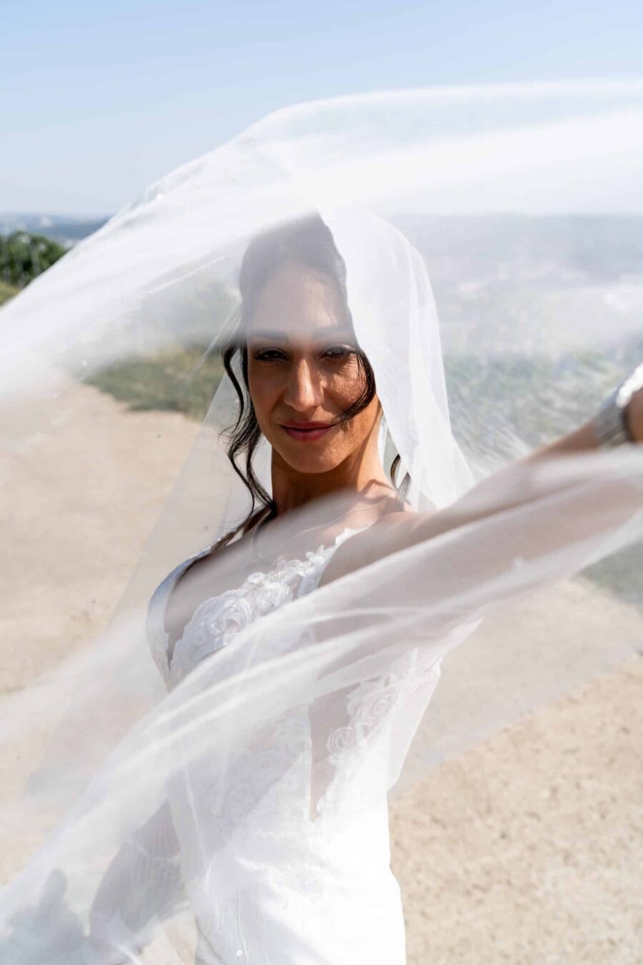 Braut lächelt unter Schleier bei sonniger Outdoor-Hochzeit