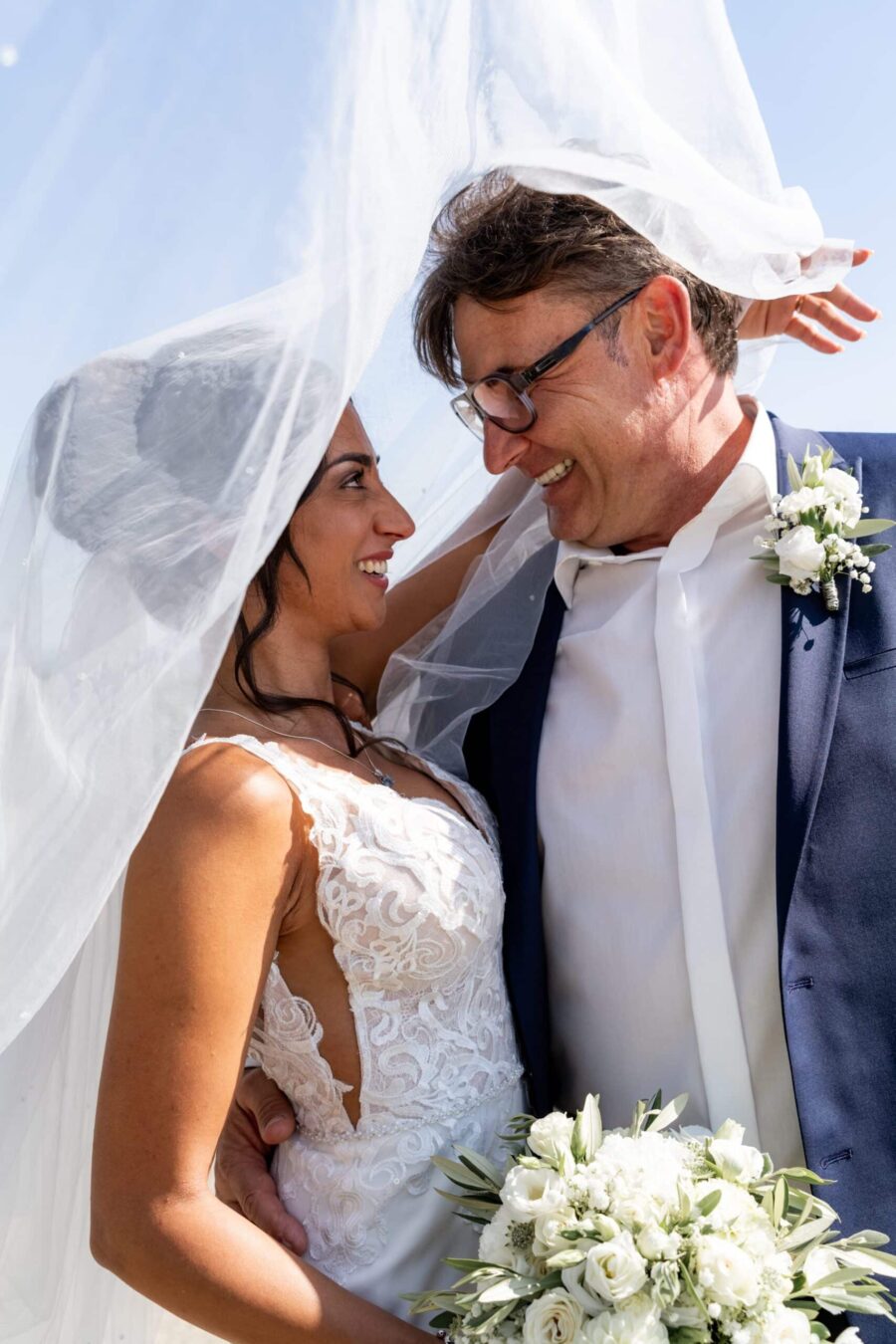 Brautpaar lächelt unter Brautschleier im Sonnenschein