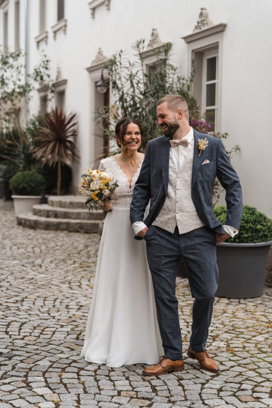 Brautpaar lachend im Hof mit Blumenstrauß