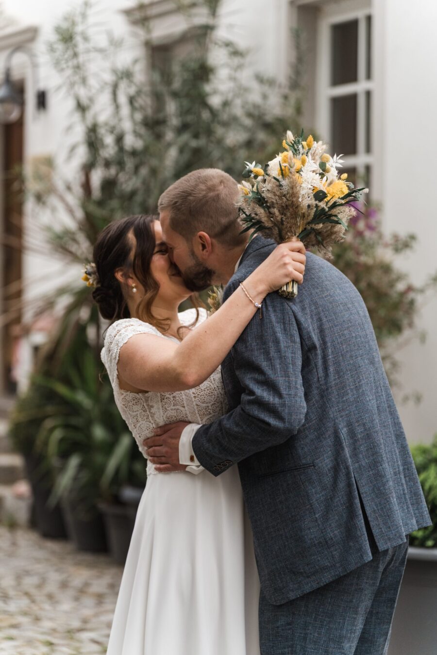 Brautpaar küsst sich im Garten mit Blumenstrauß