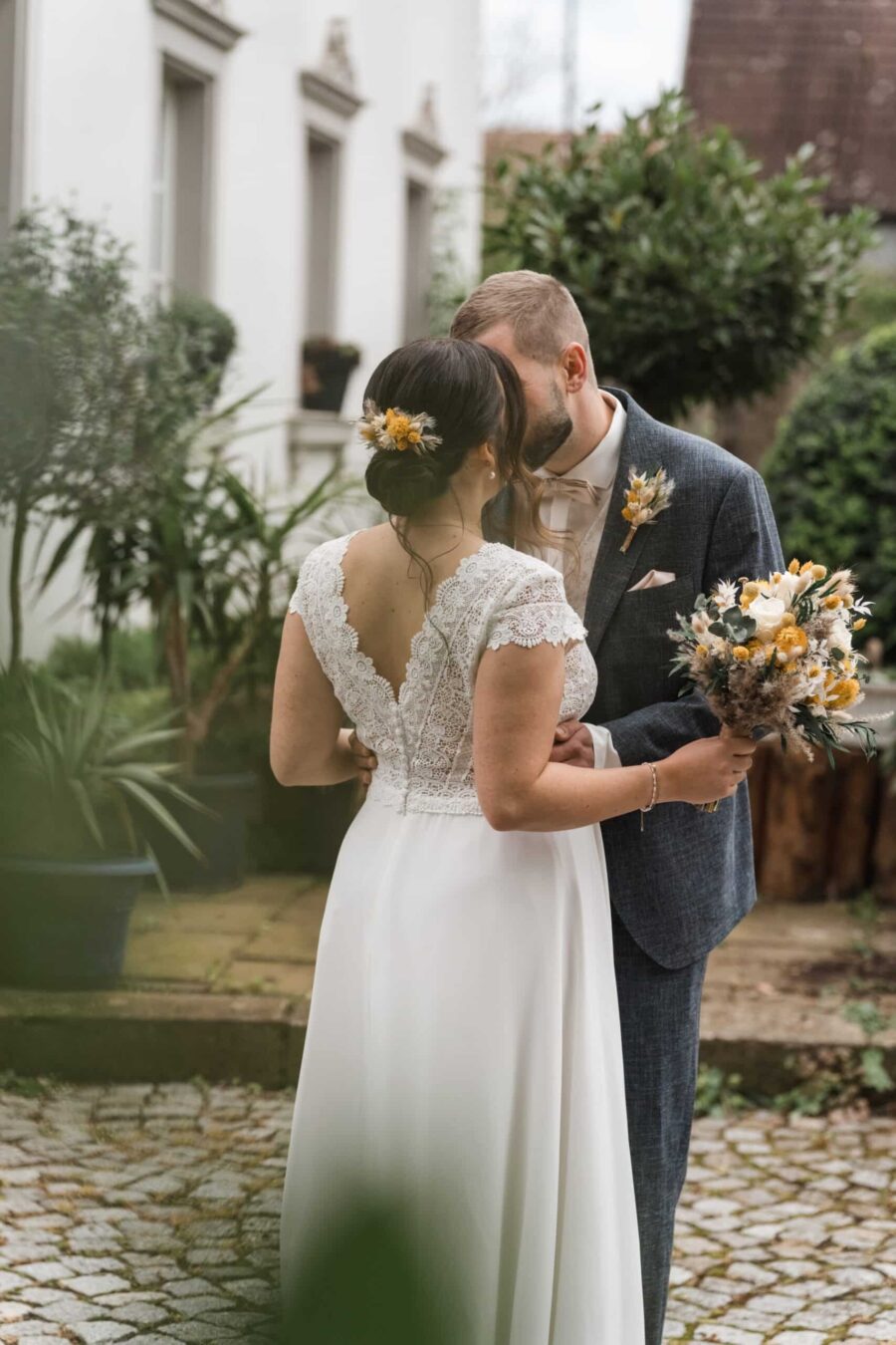 Brautpaar küsst sich im Garten mit Blumenstrauß