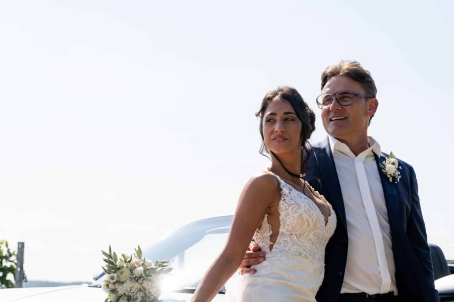 Brautpaar lächelnd vor Hochzeitsauto im Freien