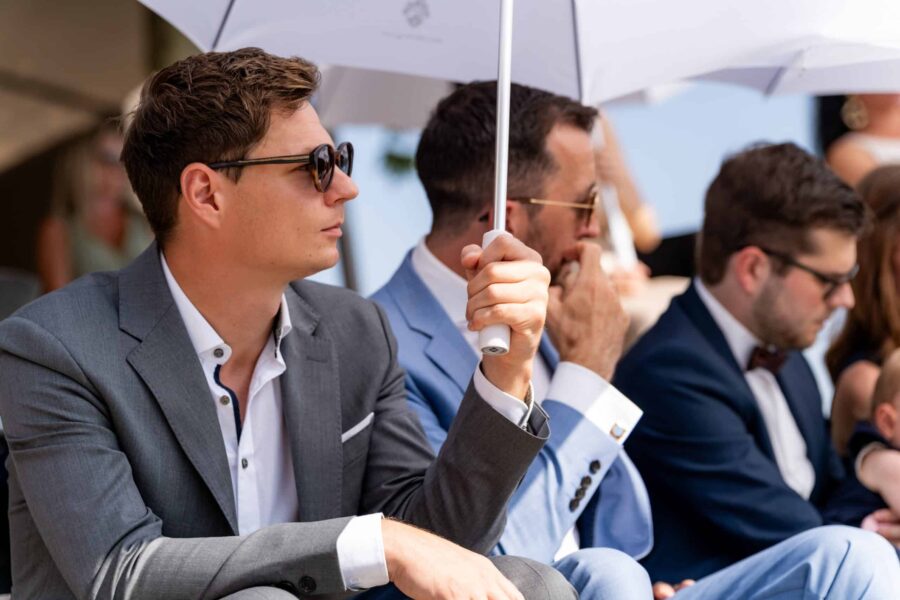 Gäste in Anzügen mit Sonnenschirmen auf Hochzeit