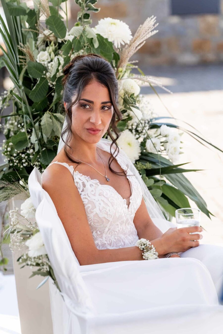 Braut in weißem Kleid vor Blumenarrangement