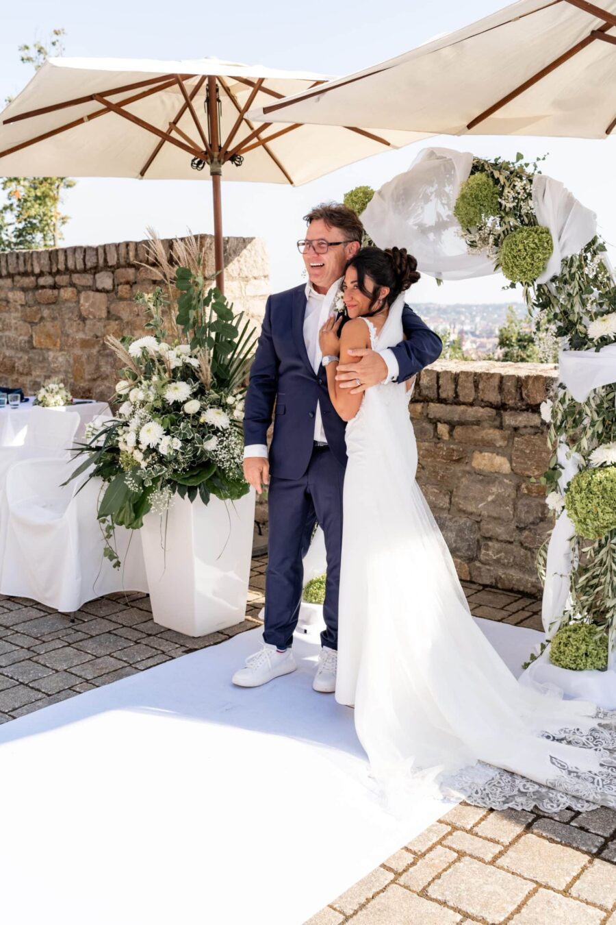 Brautpaar umarmt sich vor Blumendekoration draußen