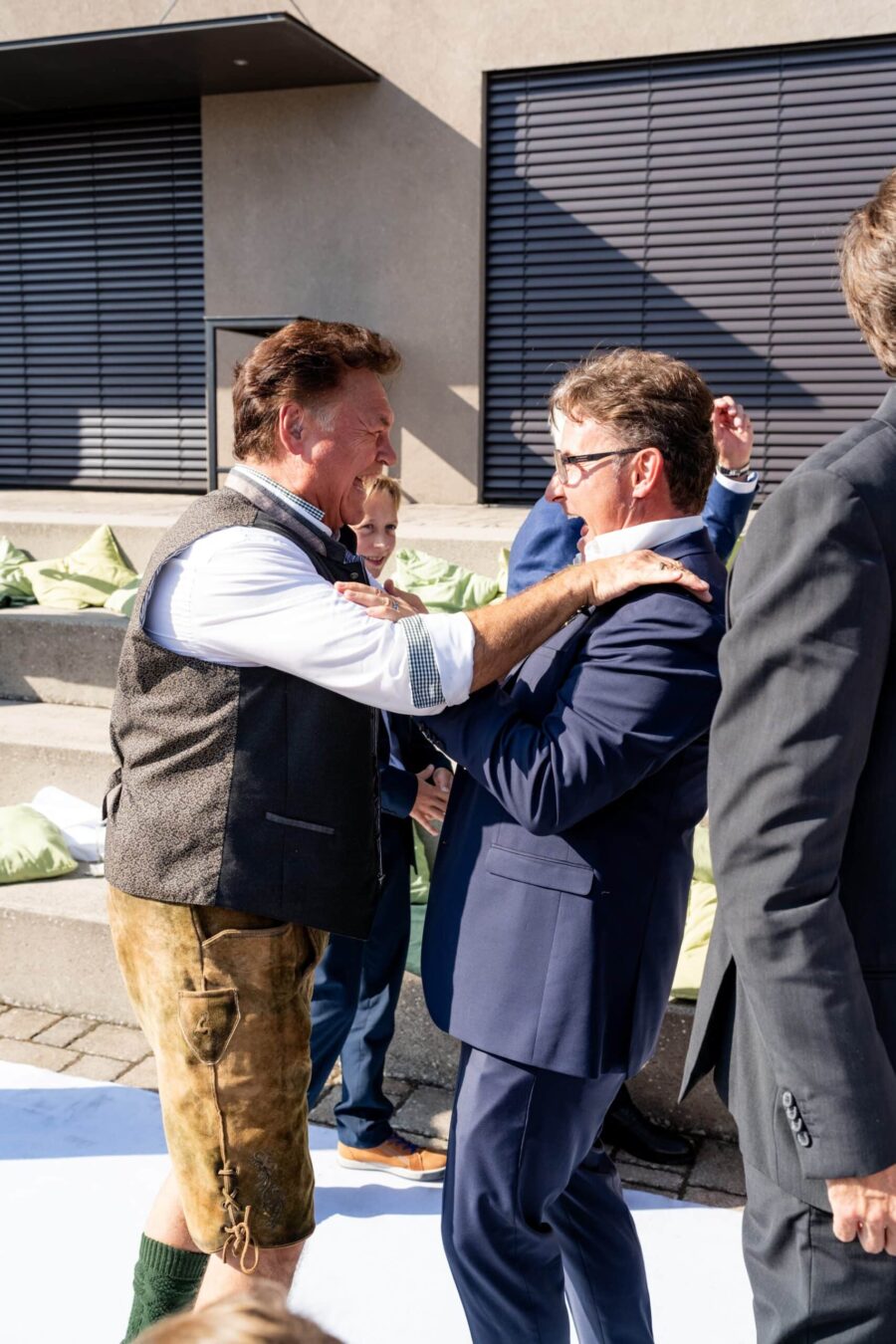 Gäste begrüßen sich fröhlich bei Hochzeit im Freien.