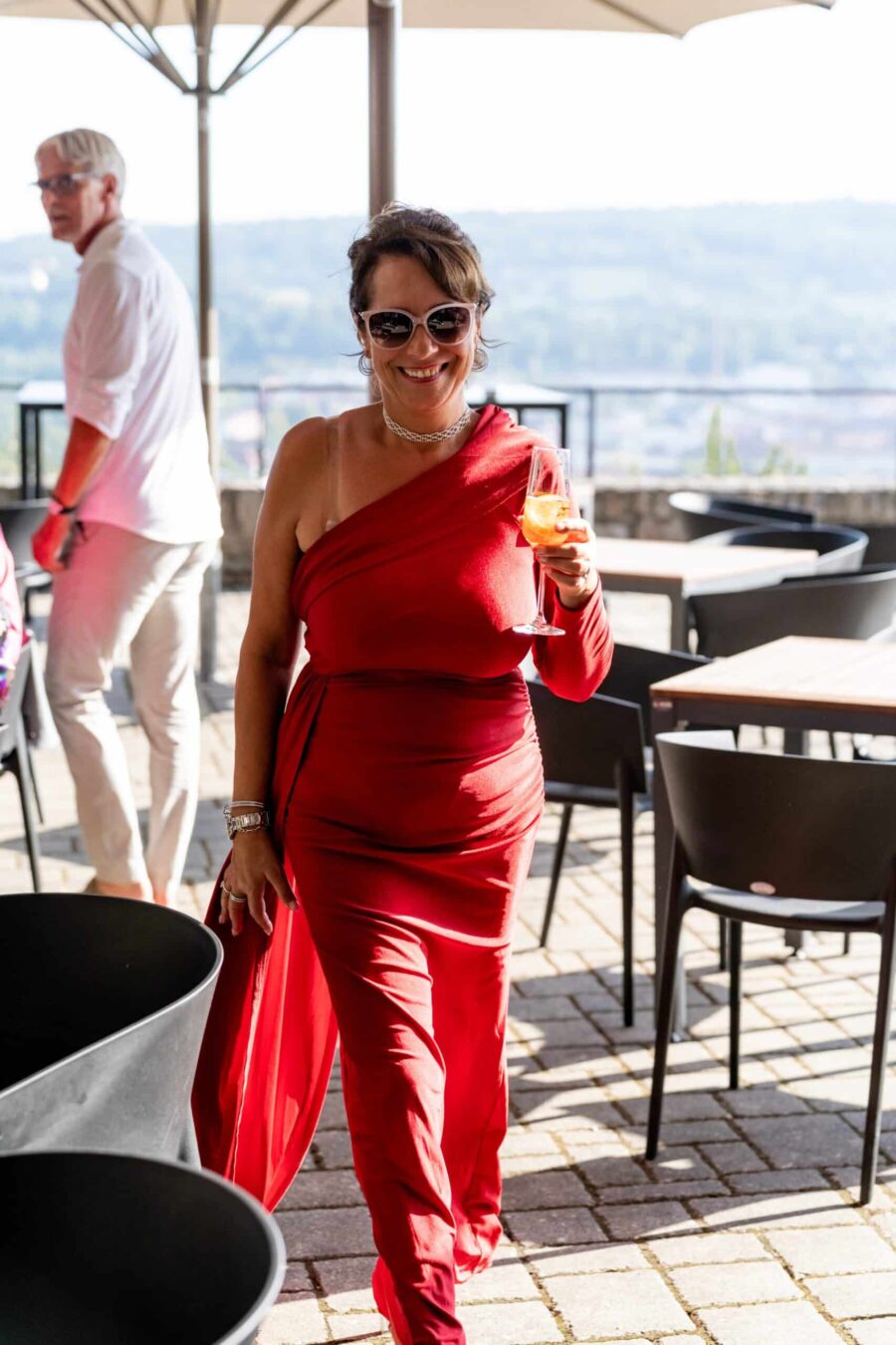 Gästin in rotem Kleid mit Getränk auf Hochzeitsterrasse