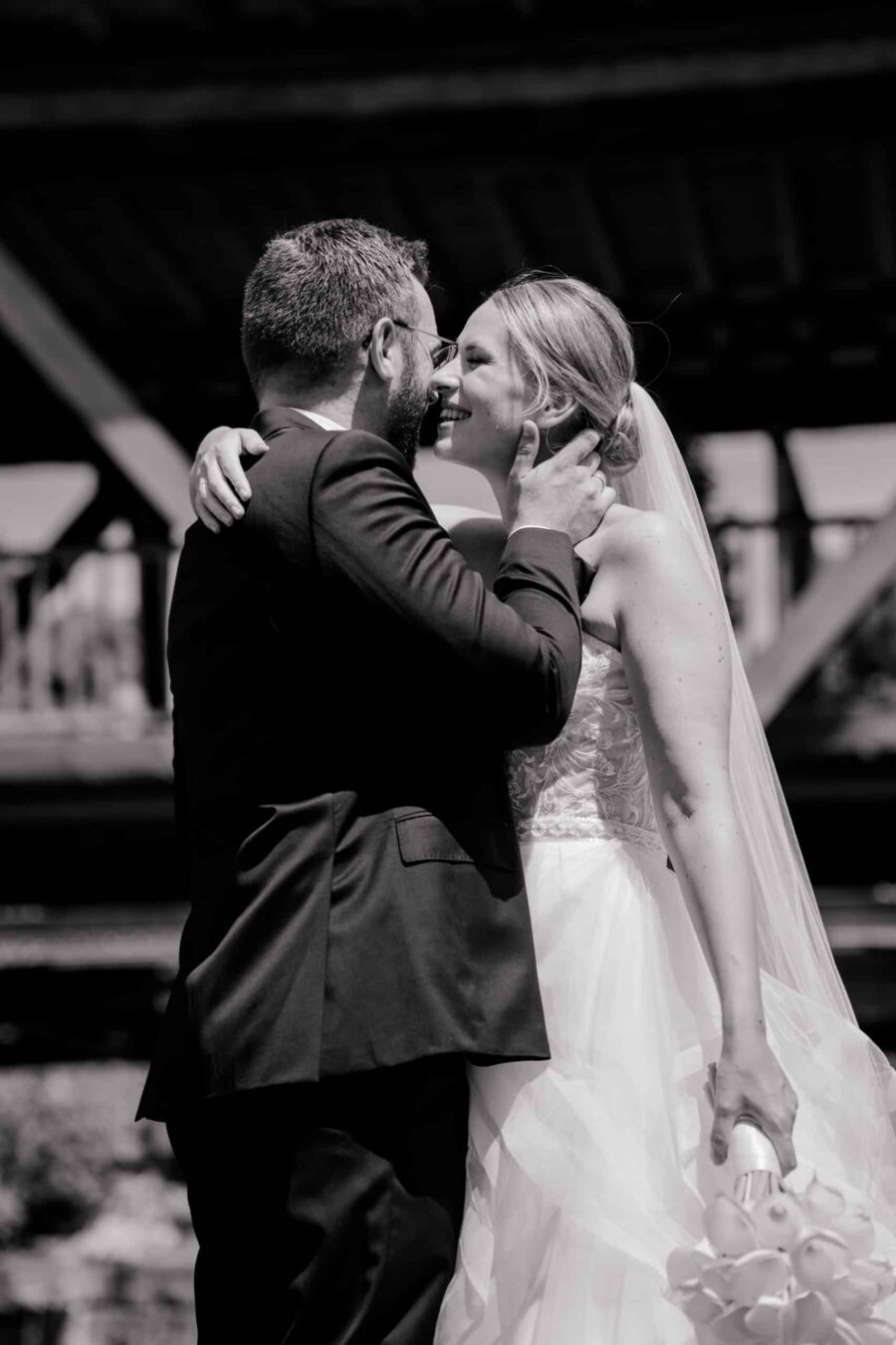 Brautpaar umarmt sich vor Holzbrücke