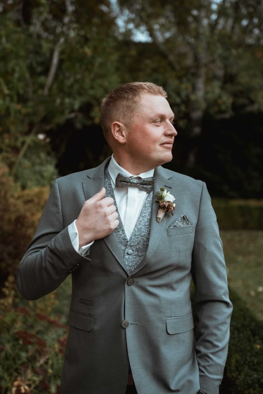 Bräutigam in grauem Anzug im Garten.