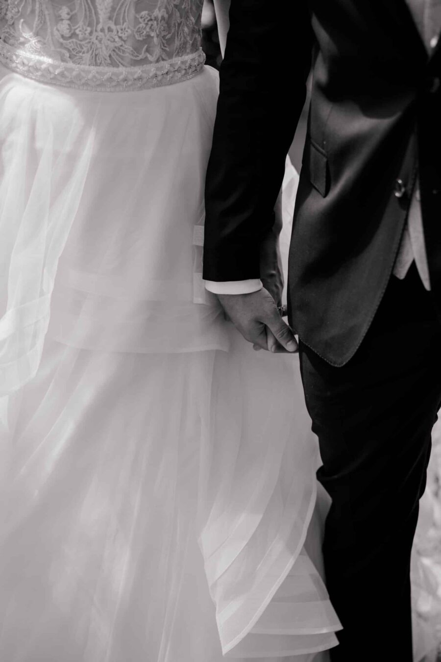 Brautpaar hält Hände in eleganter Hochzeitskleidung